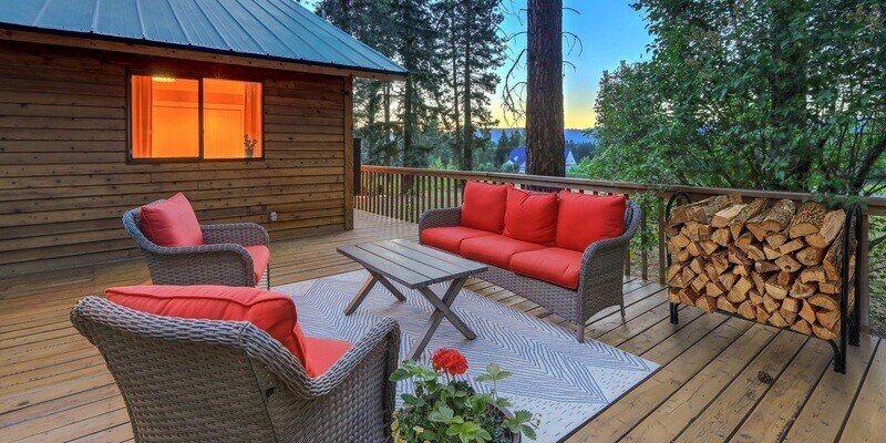 A picturesque backyard porch of a log-cabin-style home in the Rockies. There is patio furniture present, and a Shelter firewood rack loaded with wood.