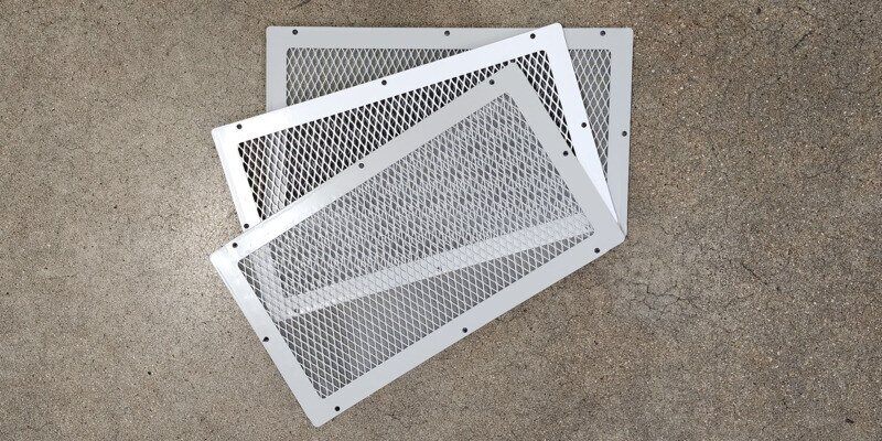 Three HY-GUARD EXCLUSION Foundation Vent Covers fanned out and lying on a concrete floor. Two are gray, and the one in the middle is white.