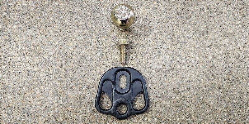 The hex head bolt, tow ball, and plate of the Hitchin' Post Plus laid out against a concrete floor.