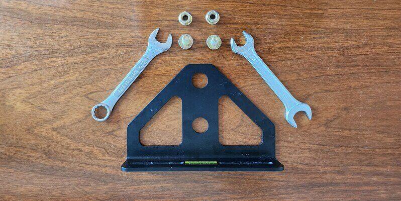 A Good Vibrations Z-Hitch Zero-Turn Hitch Plate laid out on a wooden surface. Above it are two nuts, two bolts, and two combination wrenches.