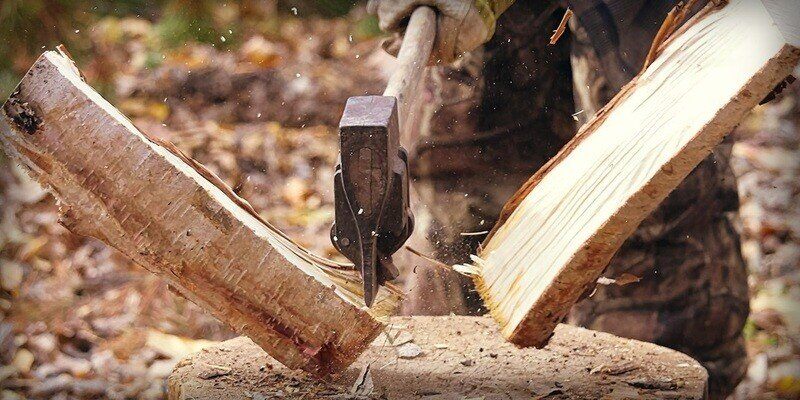 A man using an ax to split firewood. The two split pieces have just been cut and are actively flying away from one another.
