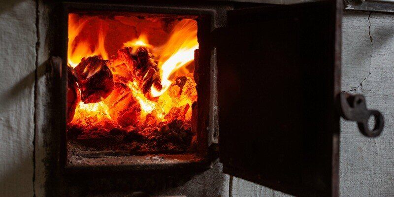 A closeup of a wood stove door open. A raging fire can be seen burning inside the stove's firebox.