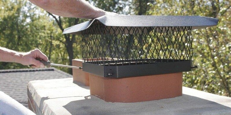 A man using a screwdriver to install a single-flue black galvanized steel chimney cap.