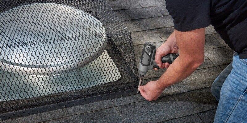 A man installing a black galvanized steel roof vent cover over a turtle-style roof vent using a gray drill.