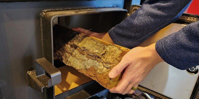 A man loading a log into the firebox of an FC1000E wood burning furnace.