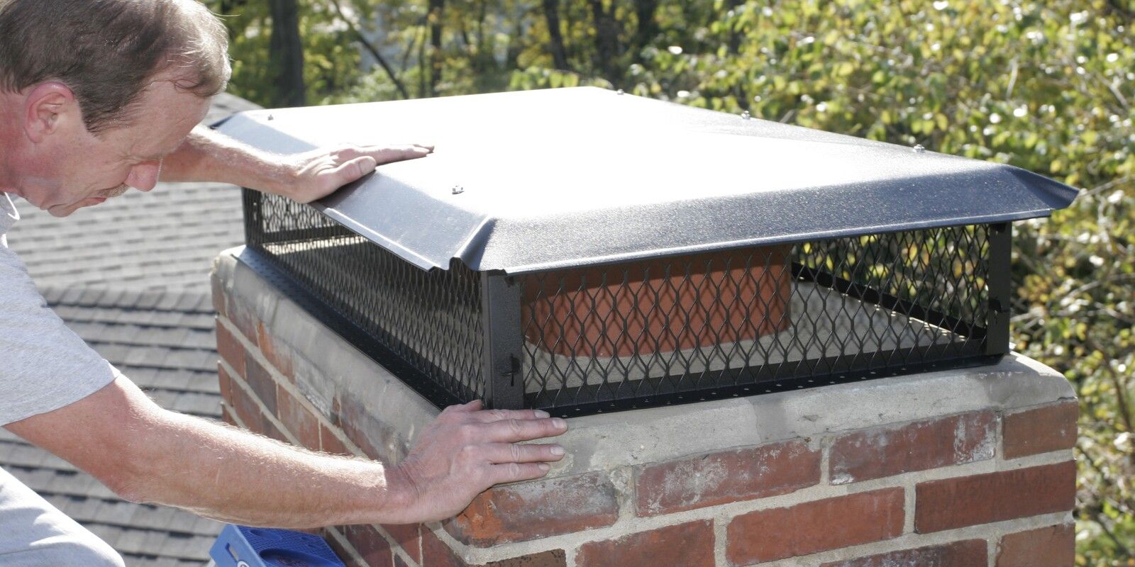 A man installing a black galvanized steel multi-flue chimney cap on a chimney crown.