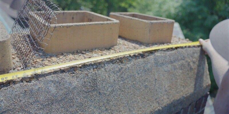 A man using a tape measure to measure the length of a multi-flue chimney's crown.