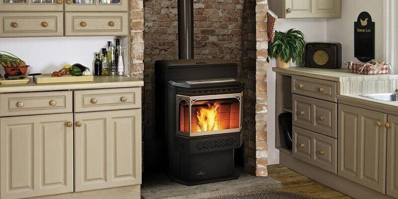 A wood pellet stove installed in a small brick inlet inside of a nice, modern-looking kitchen.