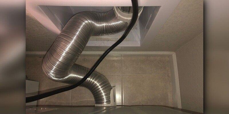 A top-down view of a recessed dryer vent box installed into a wall. A flexible vent hose attaches the dryer to the vent box.