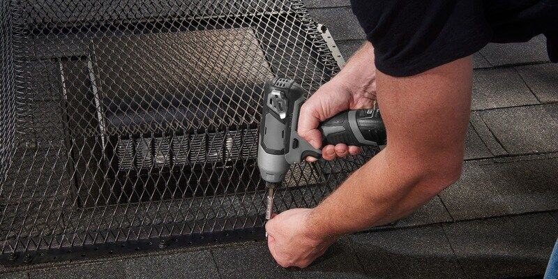A man installing a black galvanized steel HY-GUARD EXCLUSION Roof Vent Guard over a static vent on a roof with black shingles.