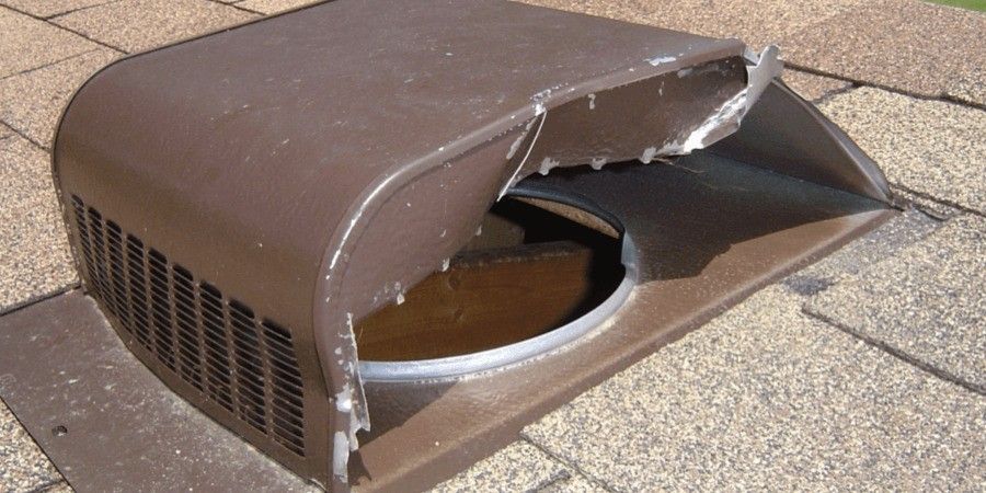 A brown box roof vent guard on a roof with tan shingles. Its side has been completely ripped off by an animal.