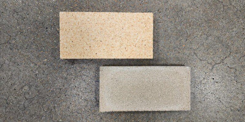 A clay firebrick and pumice firebrick from wood burning furnaces laid out on a concrete floor and photographed from above.