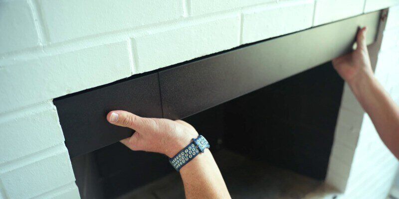 A man holding a Liberty Foundry Co. Smoke Guard against the top of his fireplace, checking it for a proper fit.