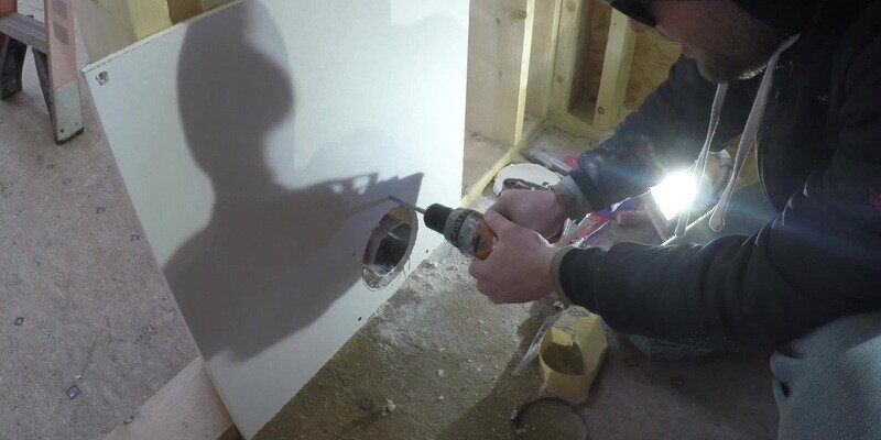 A man drilling four holes into drywall that were traced using the stencil of the SnugDryer dryer vent connector kit.