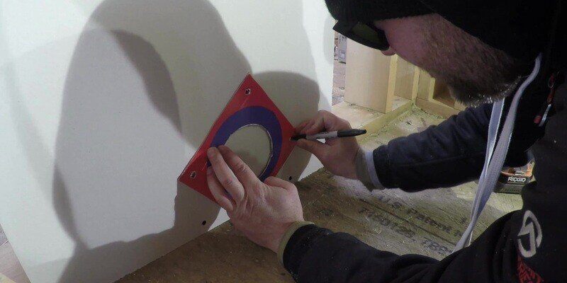 A man tracing four drill holes in the wall utilizing the SnugDryer dryer vent connector kit.