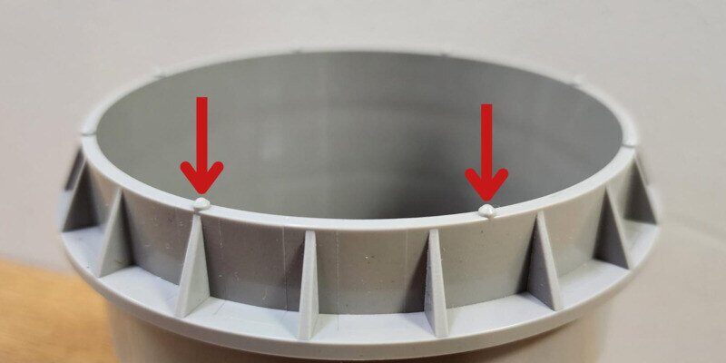 A closeup of the SnugDryer's dryer vent adapter piece. Two red arrows indicate two of the eight dimples on the end of the adapter.