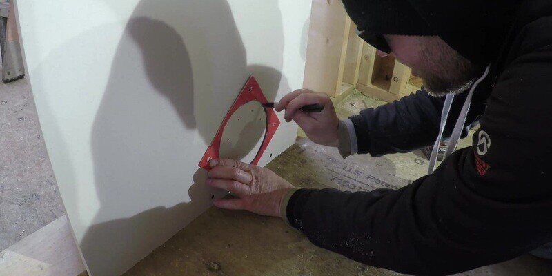 A man tracing a hole in drywall to be cut out to accommodate the back plate of a SnugDryer dryer vent connector kit.