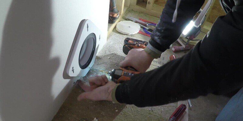 A man installing the gasket and front plate of the SnugDryer dryer vent connector kit to the drywall and back plate of the kit using four screws.