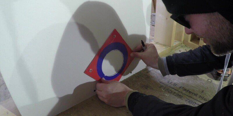 A man aligning the stencil of a SnugDryer dryer vent connector kit to the drywall of the laundry room.