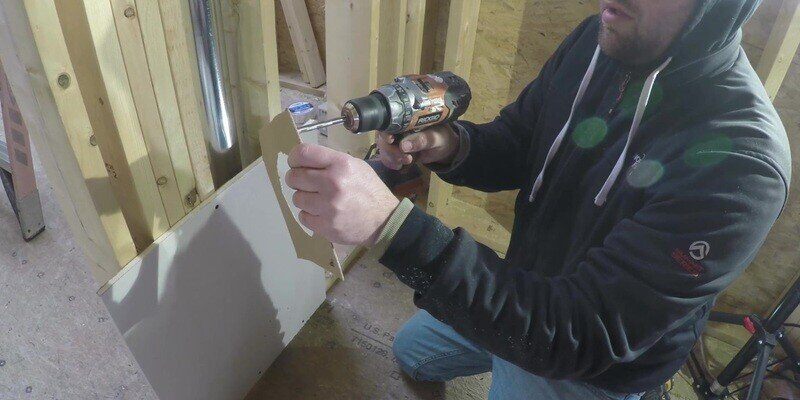 A man using a drill to drill four holes in the stencil of a SnugDryer dryer vent connector kit.