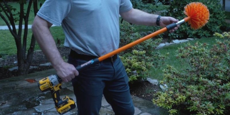 A man holding a SpinAway rotary cleaning brush. The tool is attached to a yellow drill.