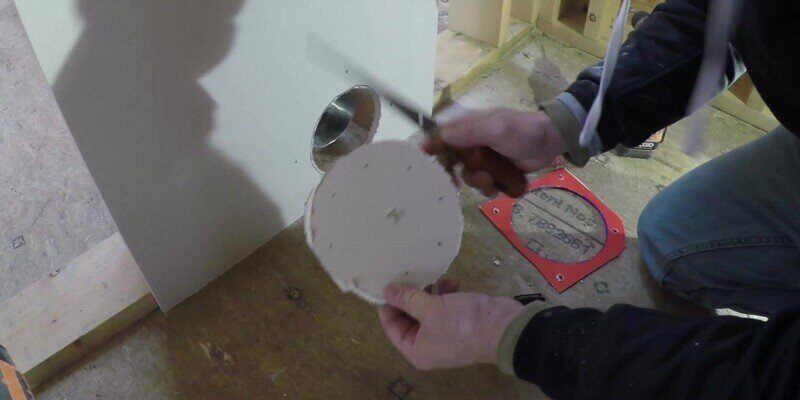A man holding a circular section of drywall he just cut out after tracing the hole using the stencil from a SnugDryer dryer vent connector kit.