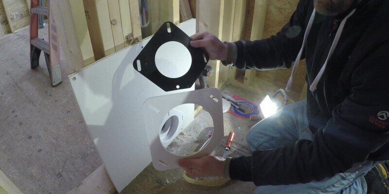 A man holding up the gasket and front plate of a SnugDryer dryer vent connector kit.