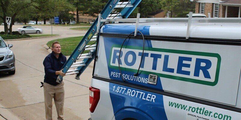 An employee of Rottler Pest Control company pulling a blue ladder down off the back of his work truck.