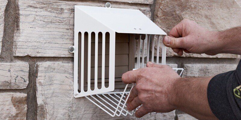 A man opening the hinged door on a HY-GUARD EXCLUSION Code Compliant Steel Dryer Vent Cover installed over a dryer vent.