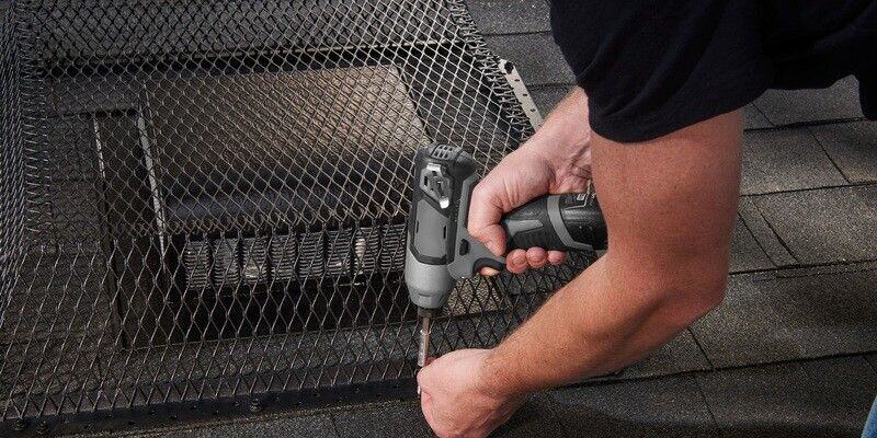 A man installing a HY-GUARD EXCLUSION roof vent guard on a roof over a roof vent. He is using a gray and black drill.