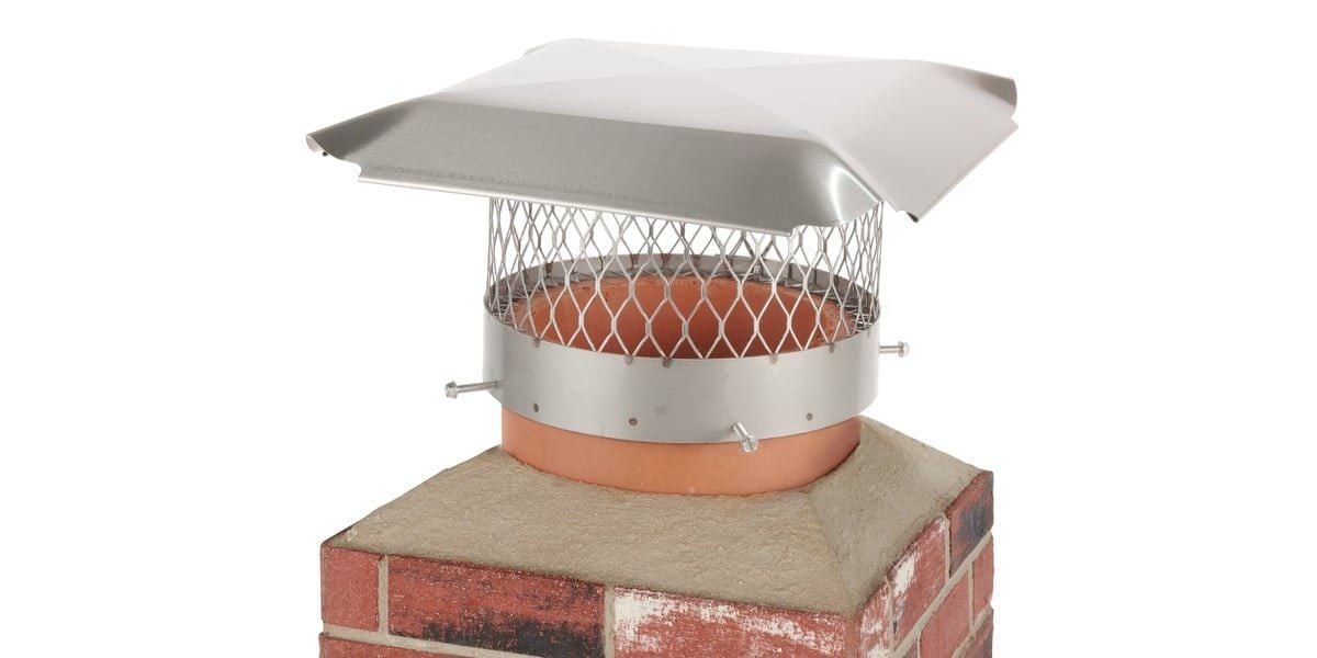 A round stainless steel Draft King chimney cap installed on a mock chimney flue against a white background.