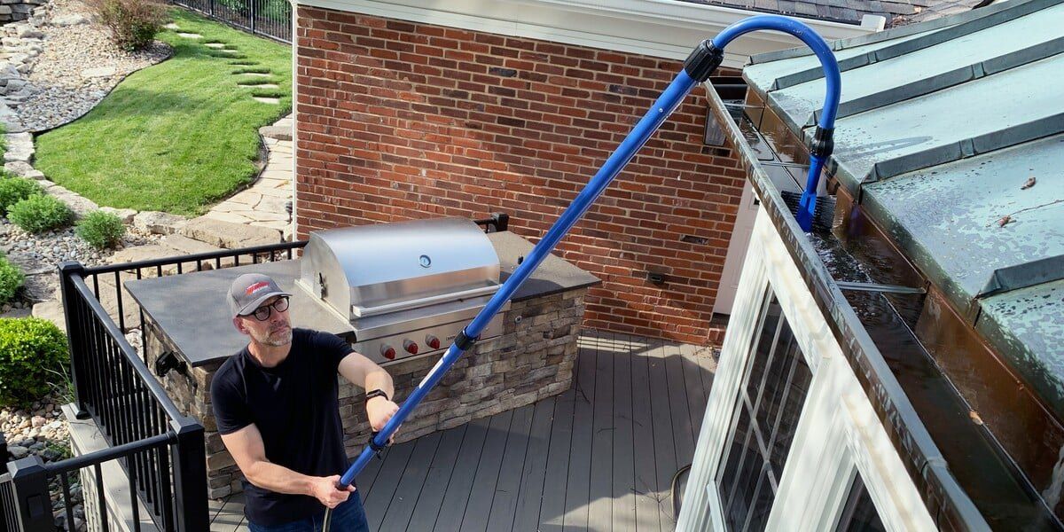 A man standing on a back patio using a GutterSweep gutter cleaning kit to clean his gutters.