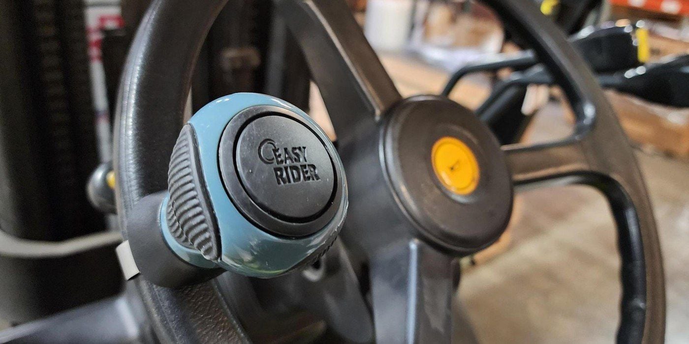 A Good Vibrations Easy-Rider Tight Turn Steering Wheel Knob installed on the wheel of a forklift parked on a factory floor.