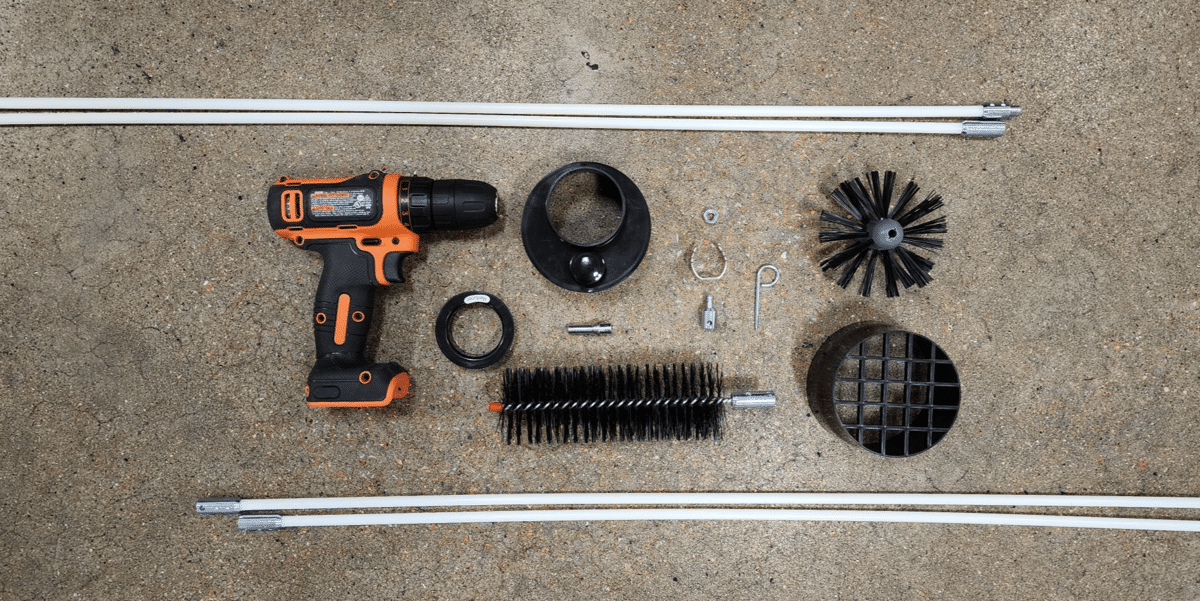 The contents of a LintEater dryer vent cleaning kit laid out next to an orange drill on a concrete floor.