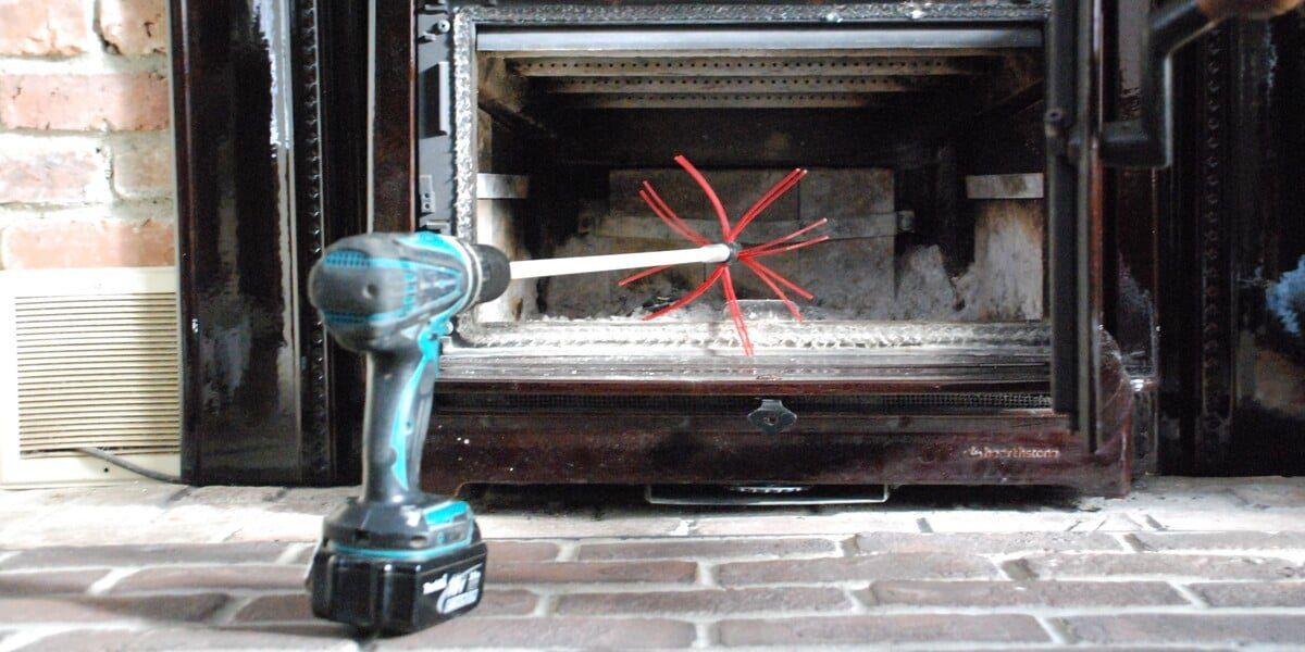 A SootEater chimney cleaning kit attached to a drill sitting on a hearth in front of an open firebox.