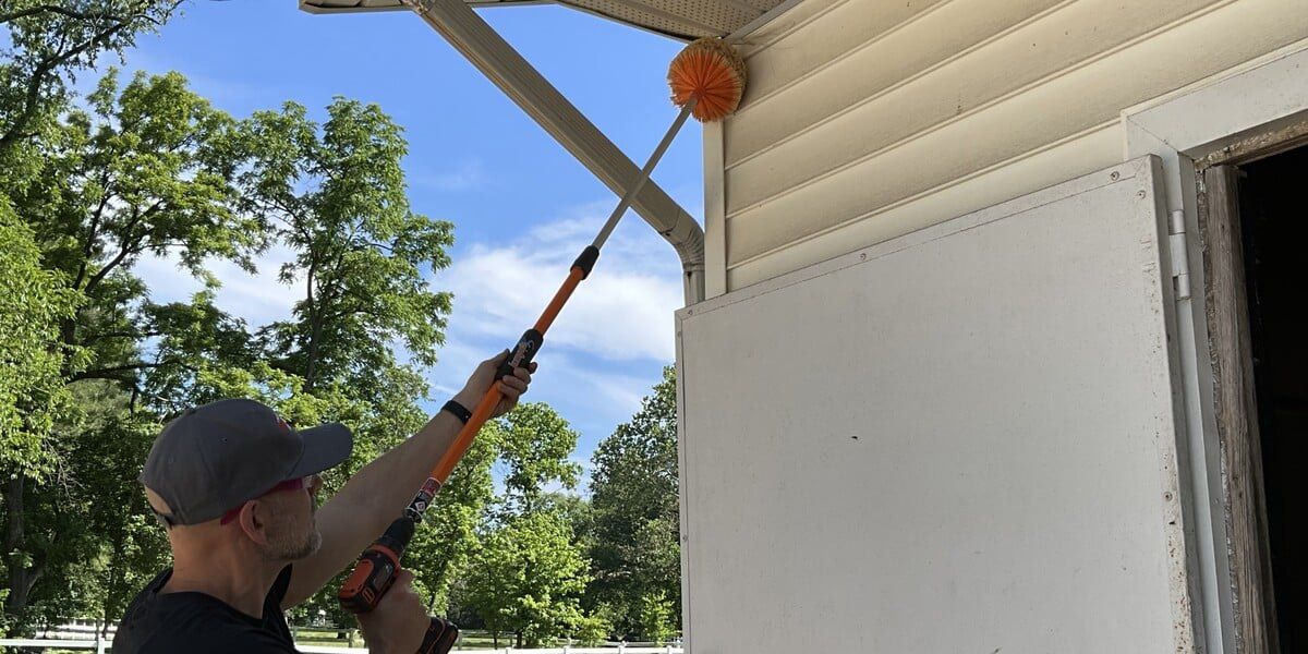 A man using a Gardus SpinAway to clean the corner of a soffit next to a downspout.