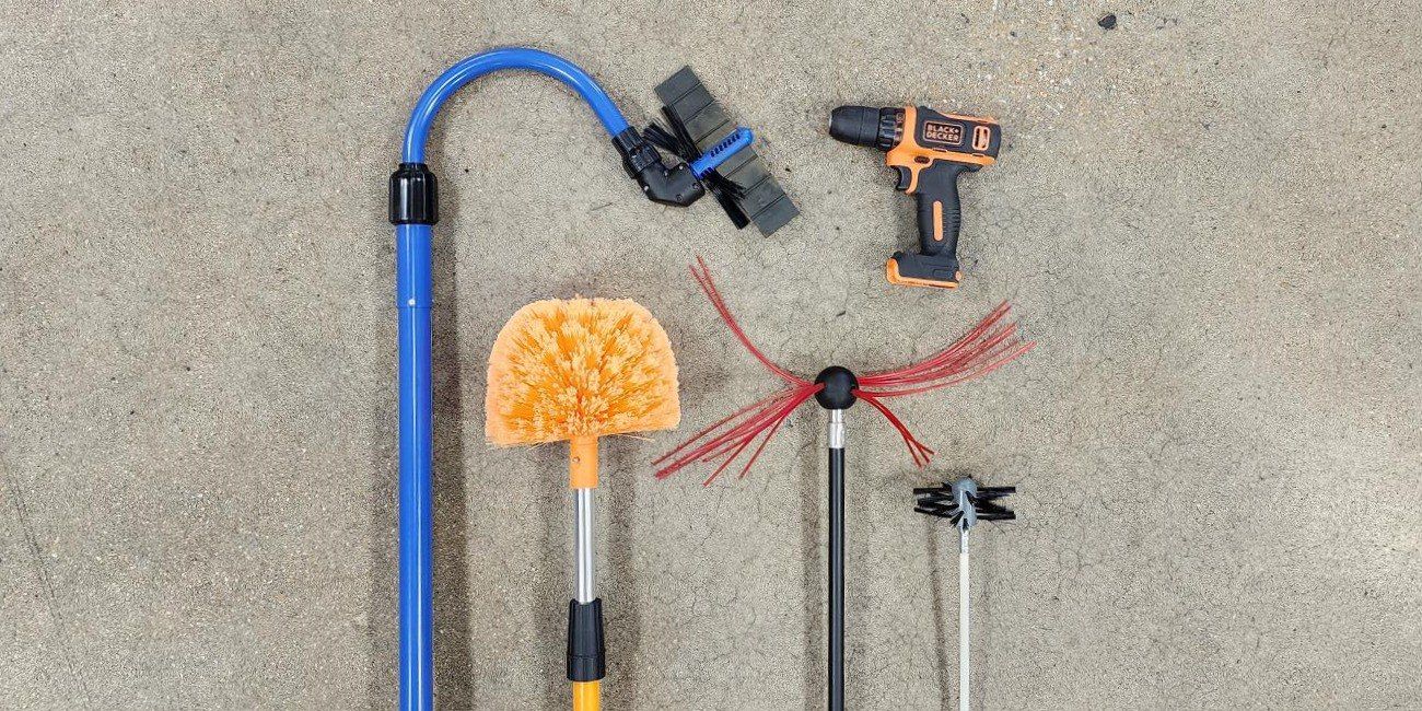 A Gardus GutterSweep, SootEater, LintEater, and SpinAway laid out next to an orange drill on a concrete floor.