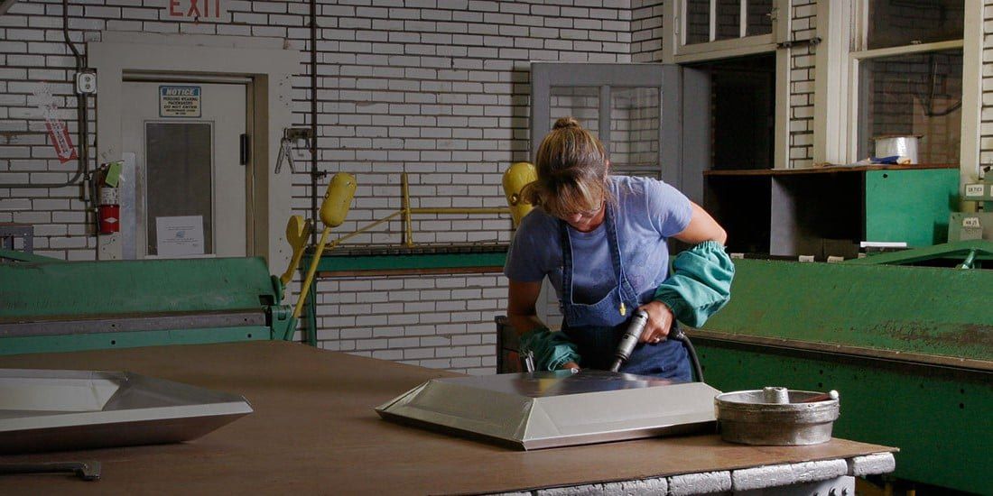 A woman holding a drill on the HY-C factory floor. She is fabricating a custom chimney cap.