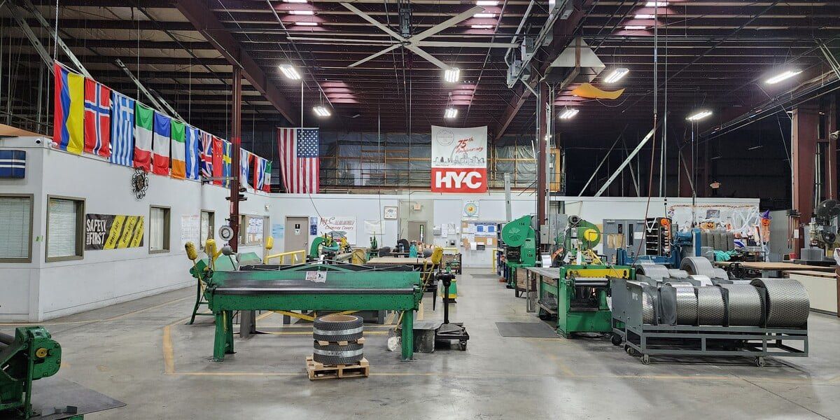 The custom chimney cap section of the HY-C factory floor adorned with banners, country flags, and industrial machinery.