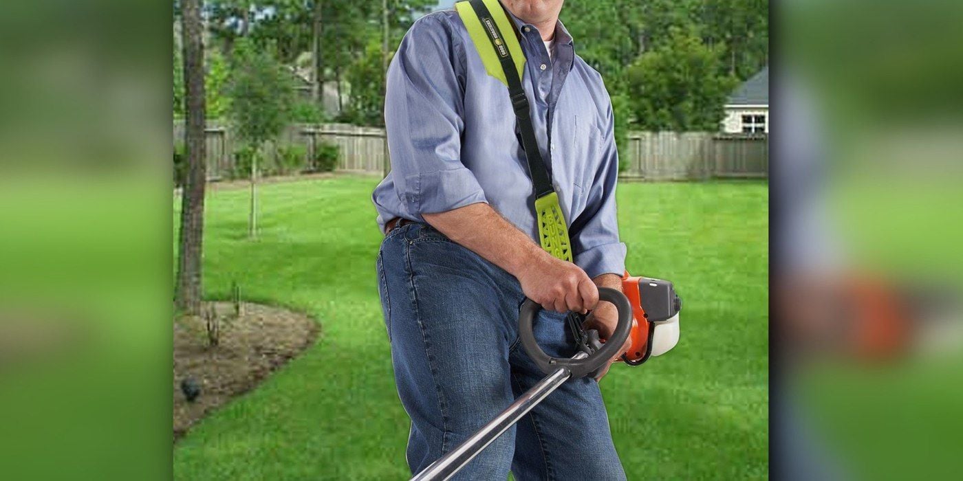 A man using a weed eater with a Good Vibrations Zero Gravity Trimmer Strap attached to it. A suburban yard is visible in the background.