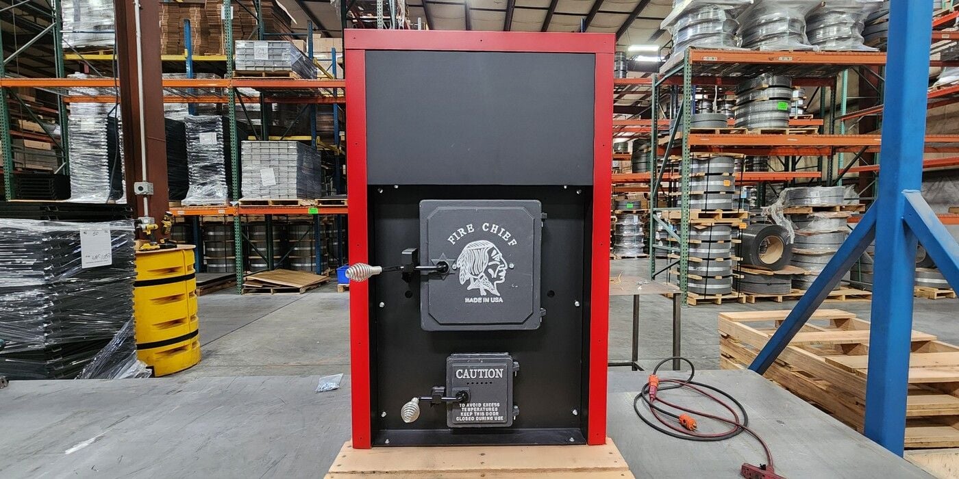 A Fire Chief FC1000E sitting on a pallet in a warehouse with shelving full of raw metal material in the background.