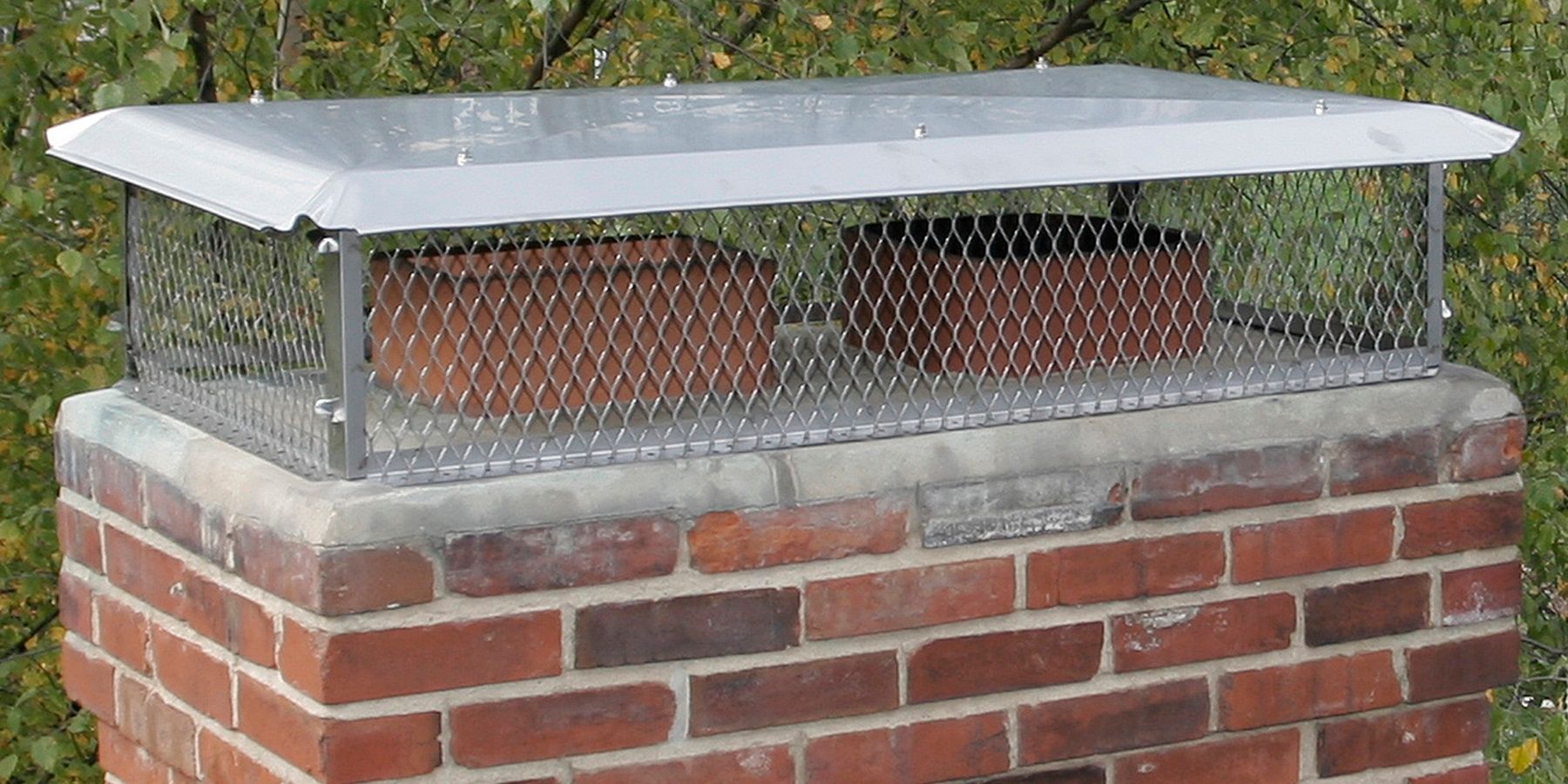 A stainless steel multi-flue chimney cap installed on a chimney with two flue pipes.
